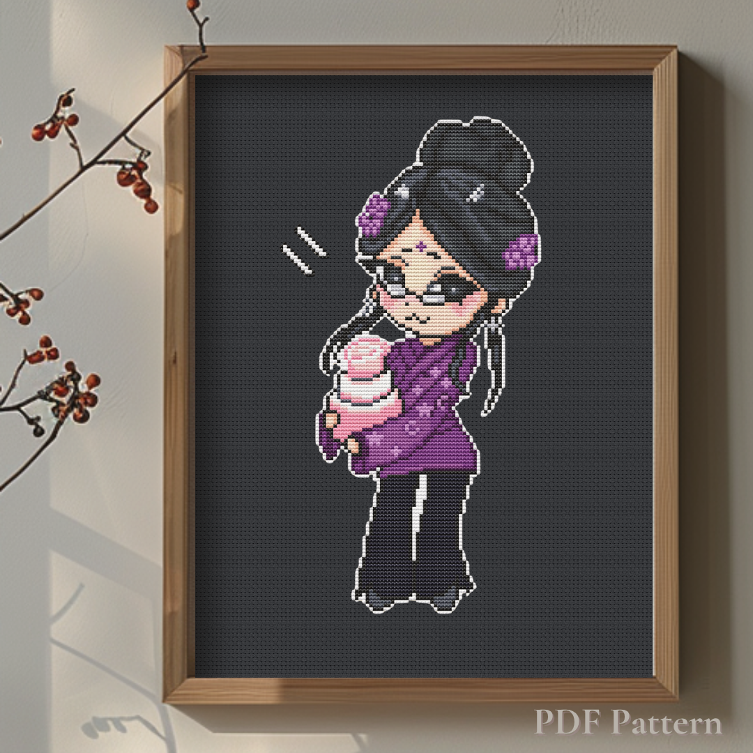 Aunt Karma cross stitch pattern displayed in a wooden frame on black fabric, highlighting the vibrant purple outfit and pink birthday cake in a warm minimalist interior.