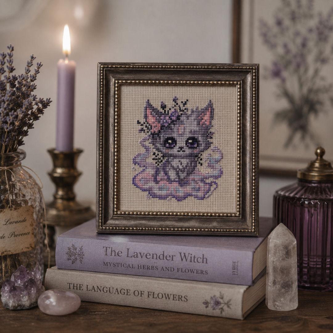 Framed cross-stitched picture of a Beastie on books with lavender and candles in the background